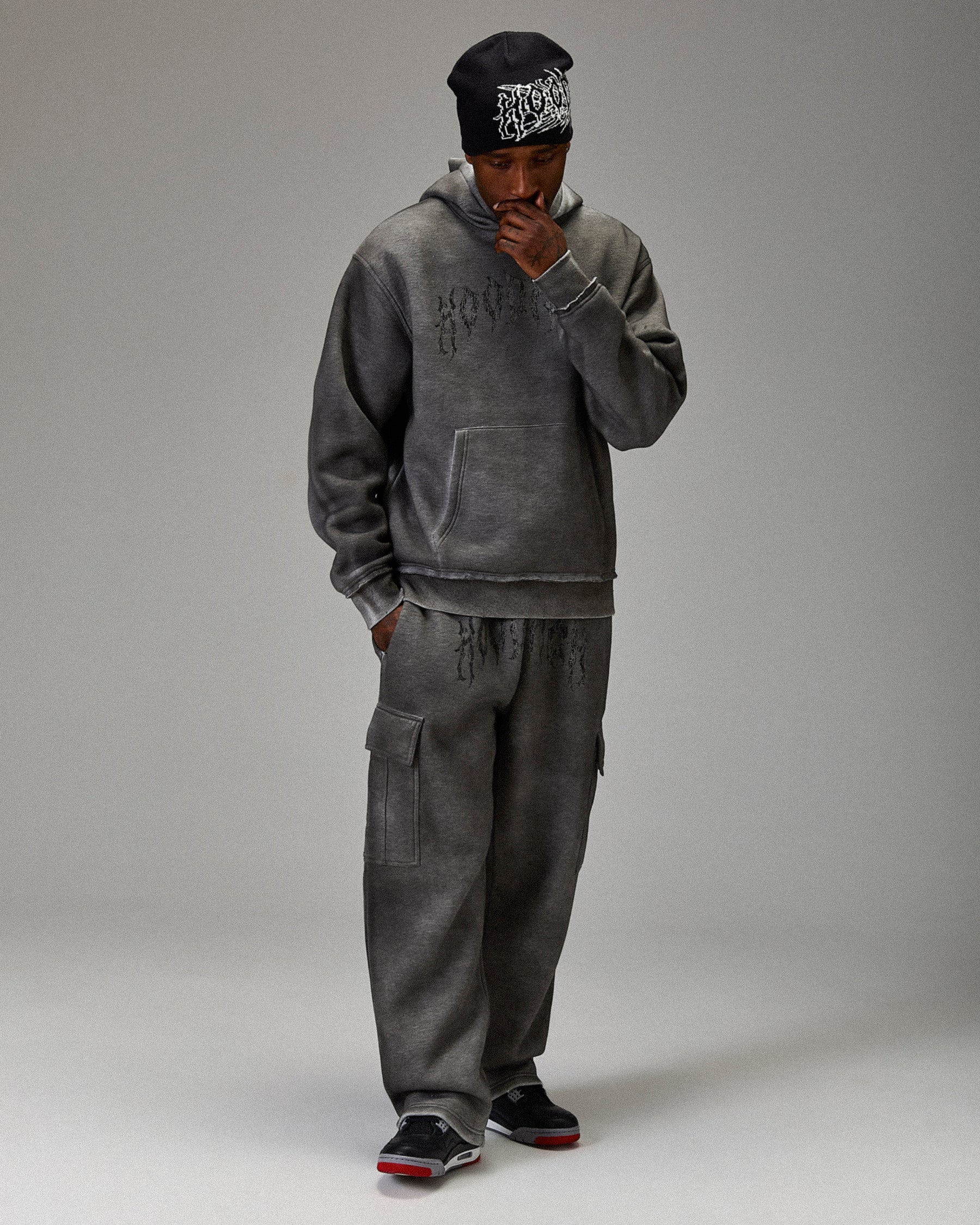 Person wearing a gray hoodie and pants with a matching beanie on a plain background