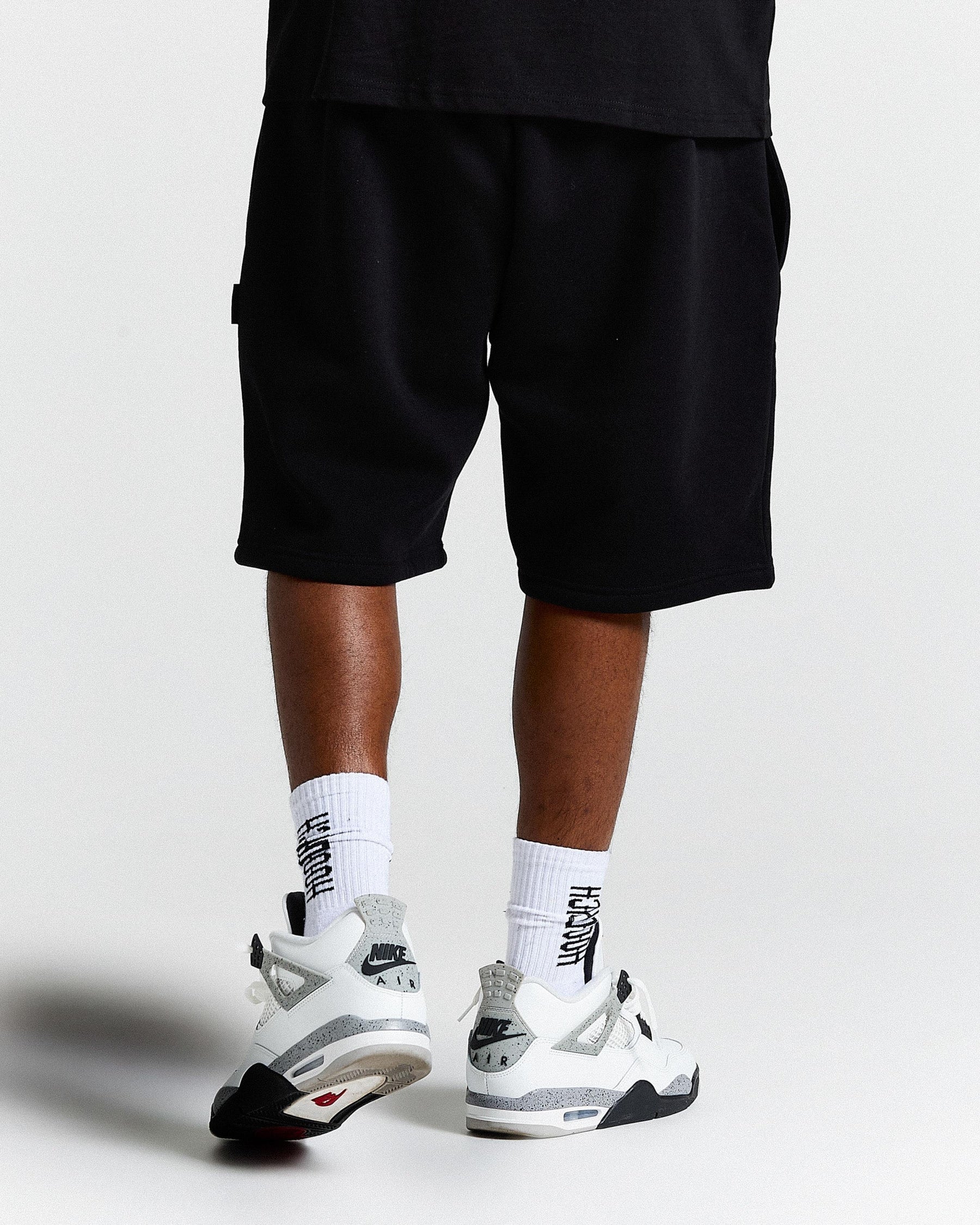 Person wearing black shorts and white sneakers on a light gray background