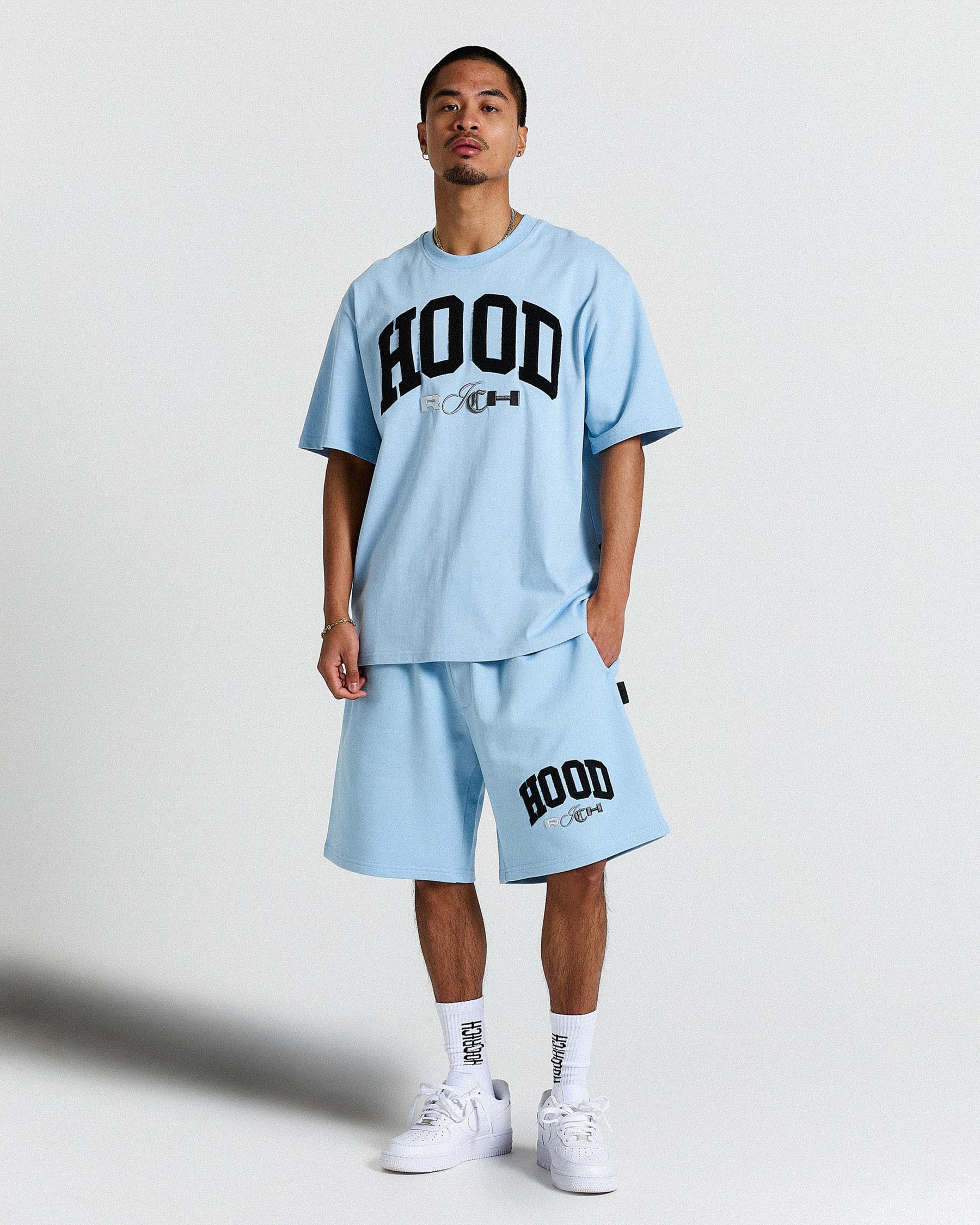 Person wearing a light blue 'HOODRICH' t-shirt and shorts set on a plain background