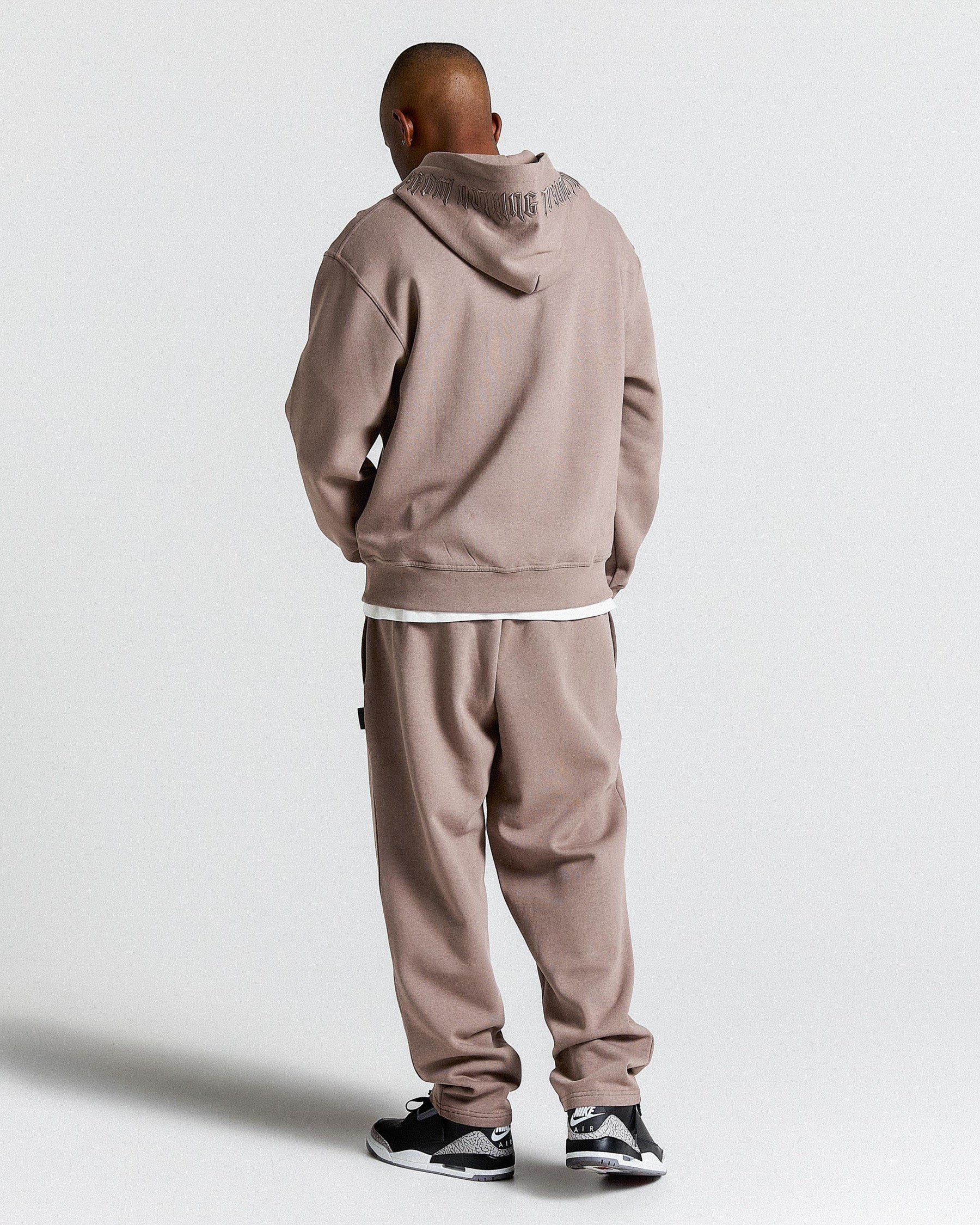 Person wearing a brown tracksuit with a hood on a white background