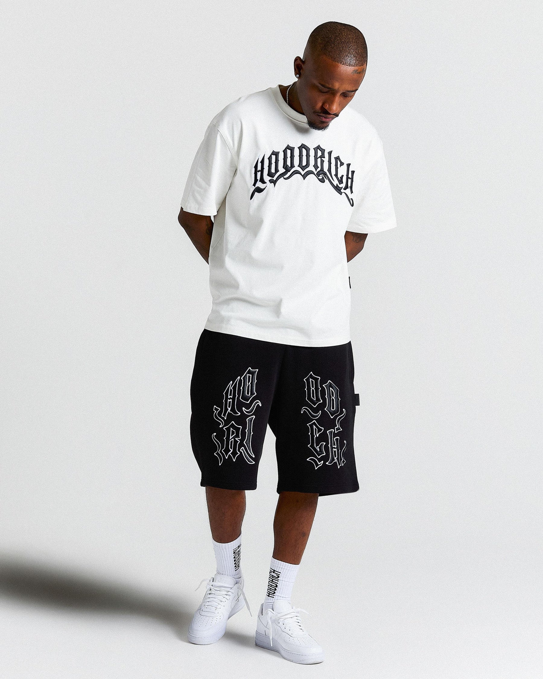 Man wearing white 'HOODRICH' branded T Shirt and black 'HOODRICH' branded shorts.