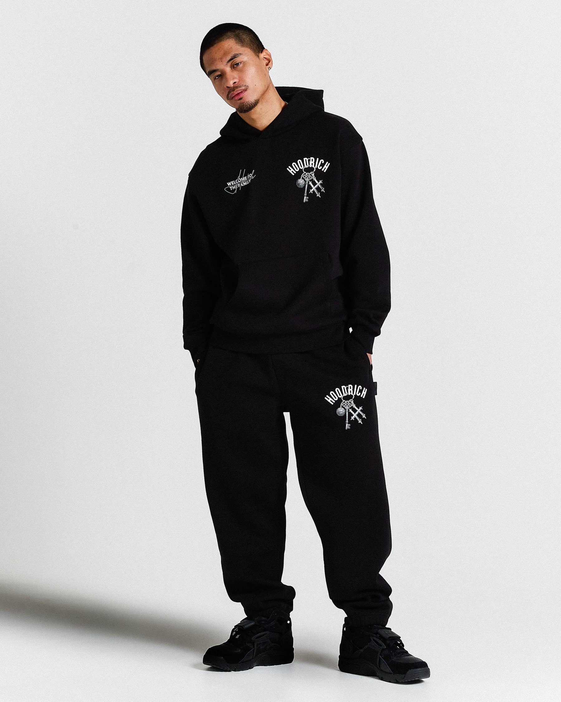 Person wearing a black hoodie and pants with branding on a white background