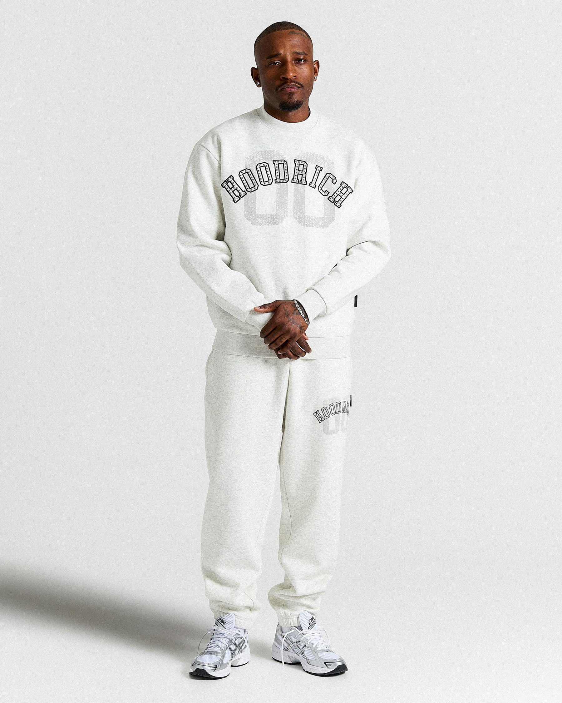 Person wearing a white 'Hoodrich' sweatshirt and pants on a light gray background