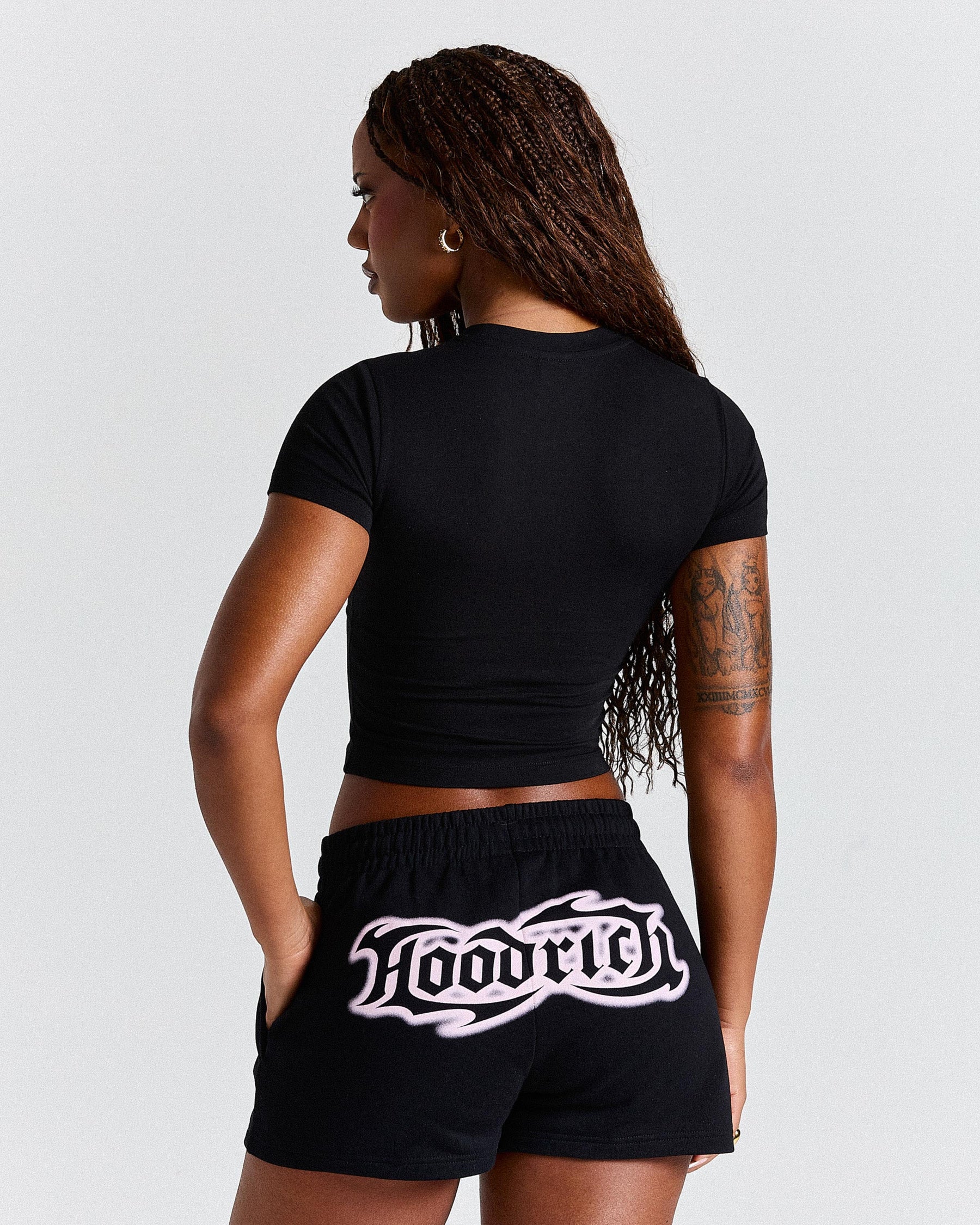 Person wearing a black crop top and black shorts with 'Hoodrich' branding on a light grey background