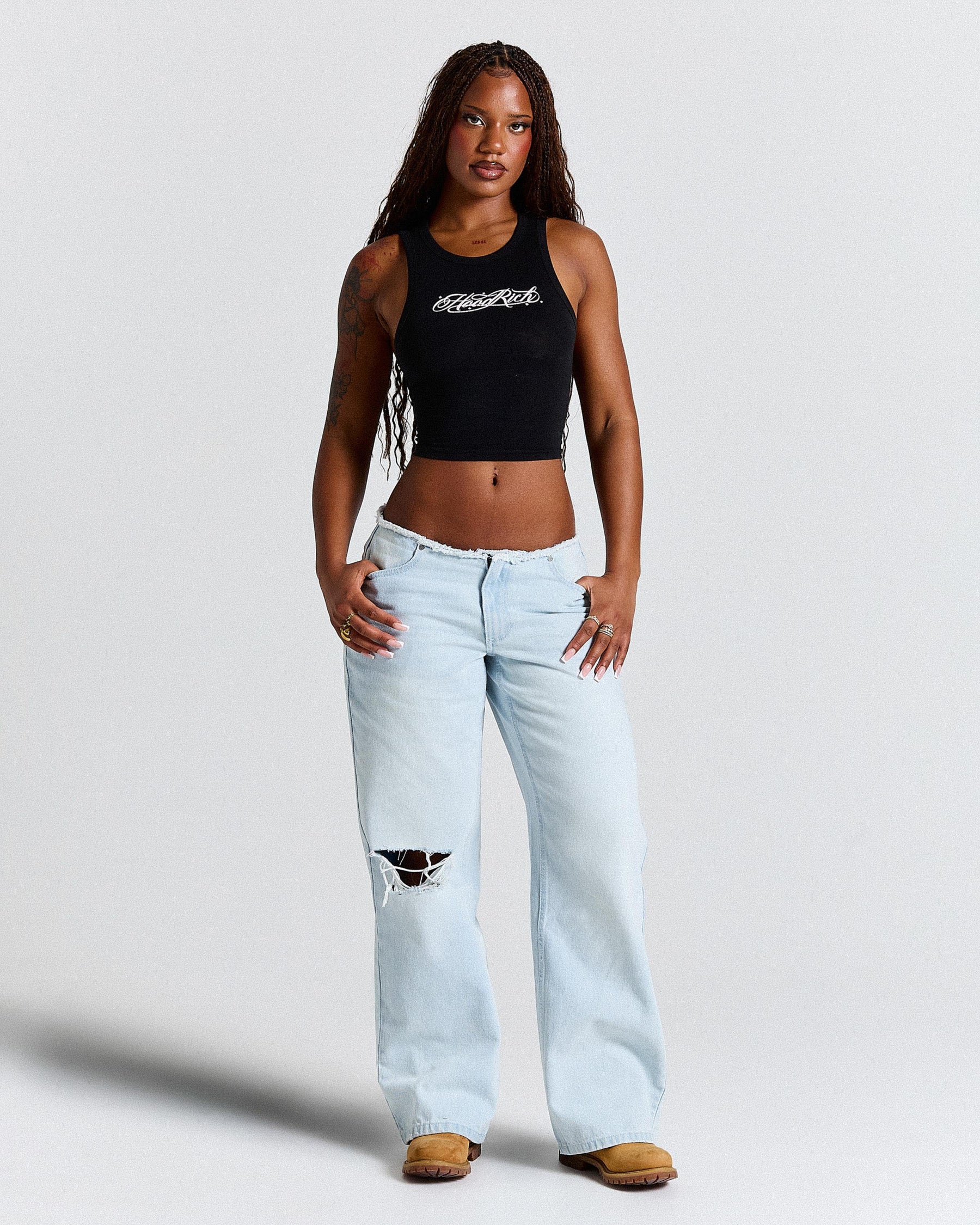 Woman wearing a black tank top and light blue jeans on a white background
