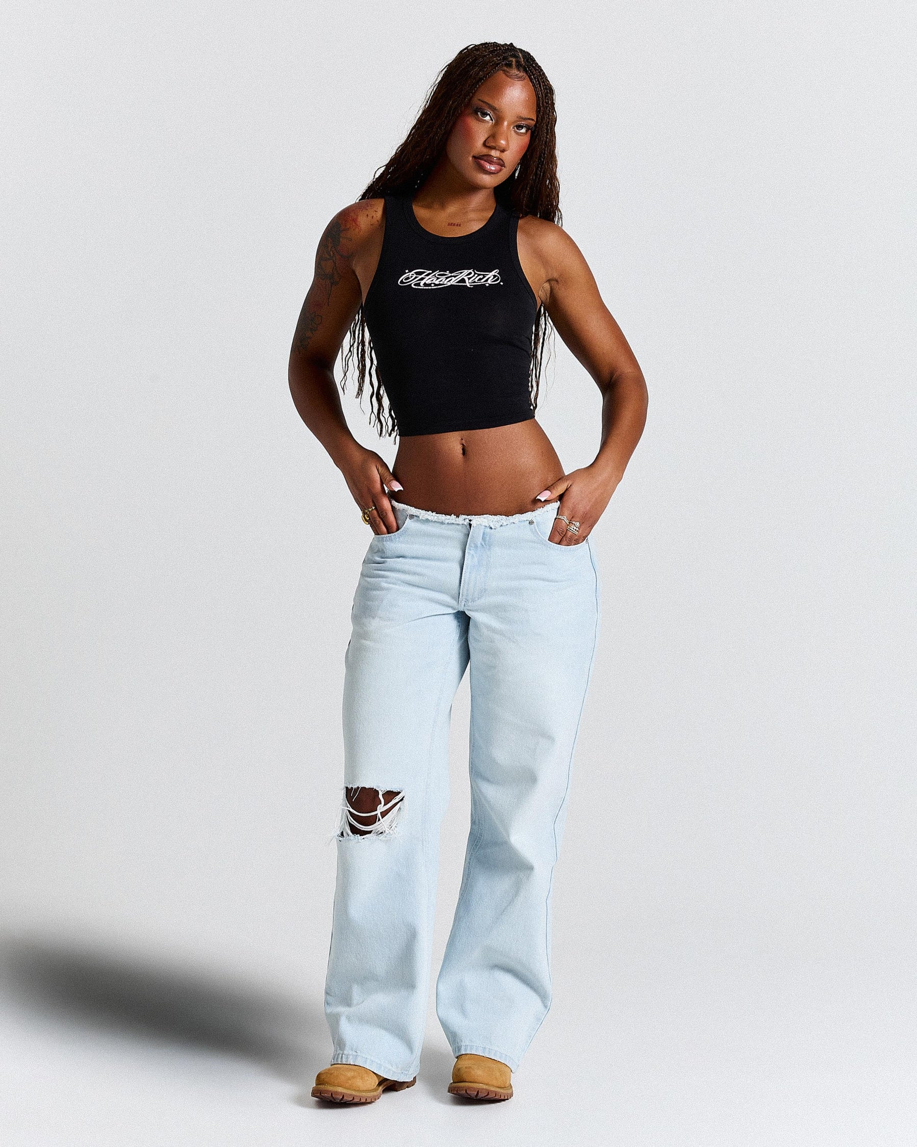 Woman wearing a black tank top and light blue jeans on a plain background