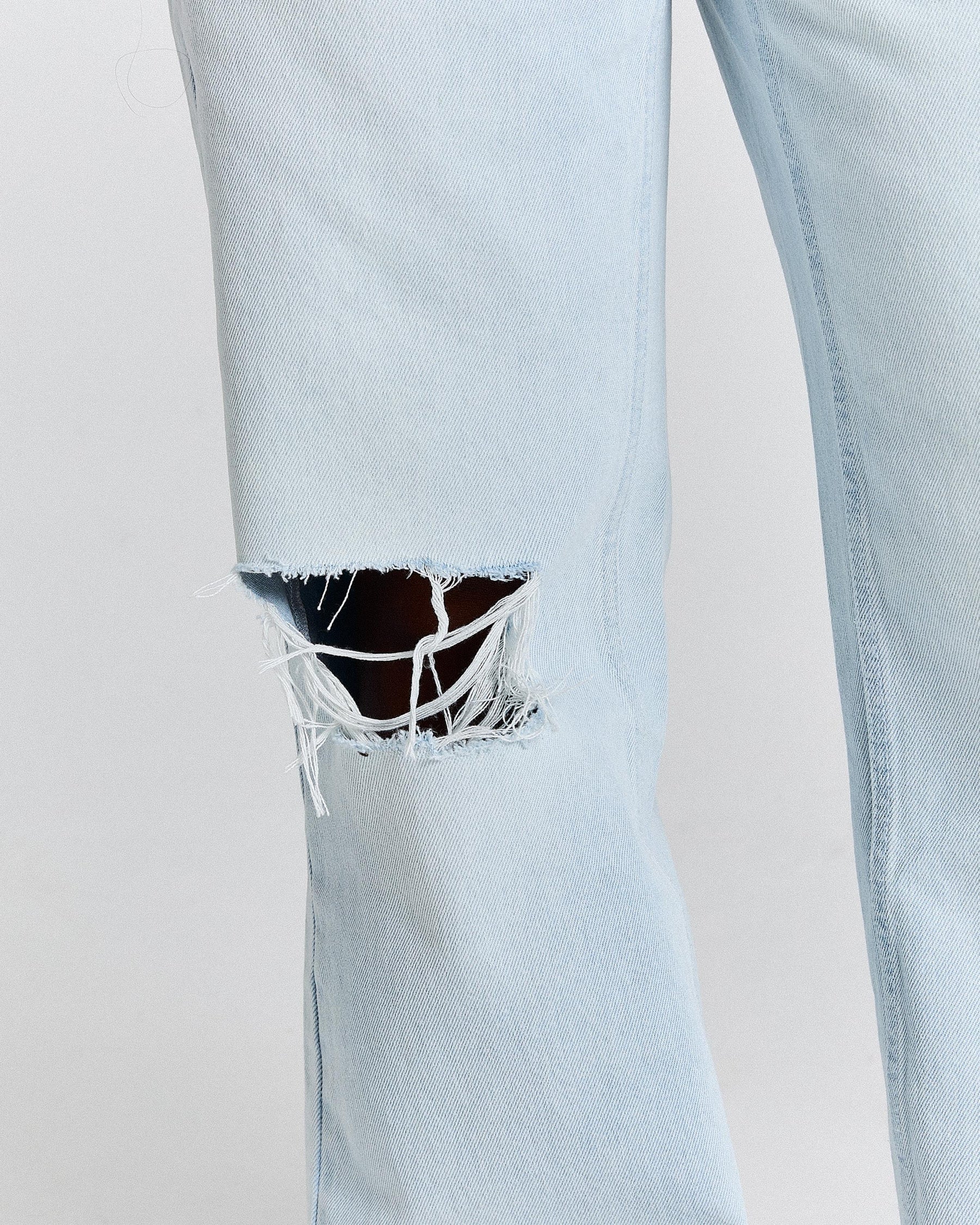 Light blue jeans with a ripped knee on a plain background