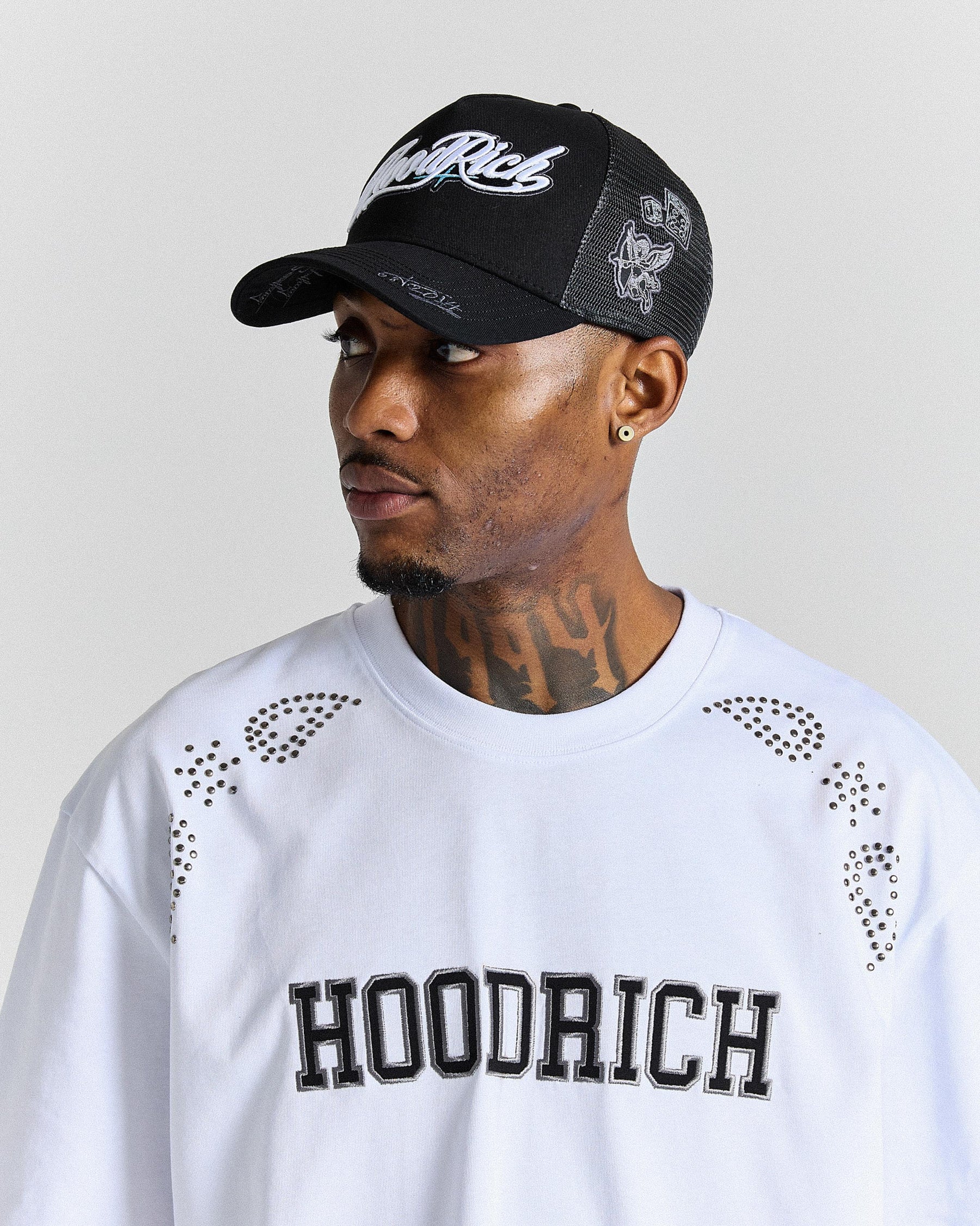 Man wearing a black cap and white 'Hoodrich' shirt against a plain background