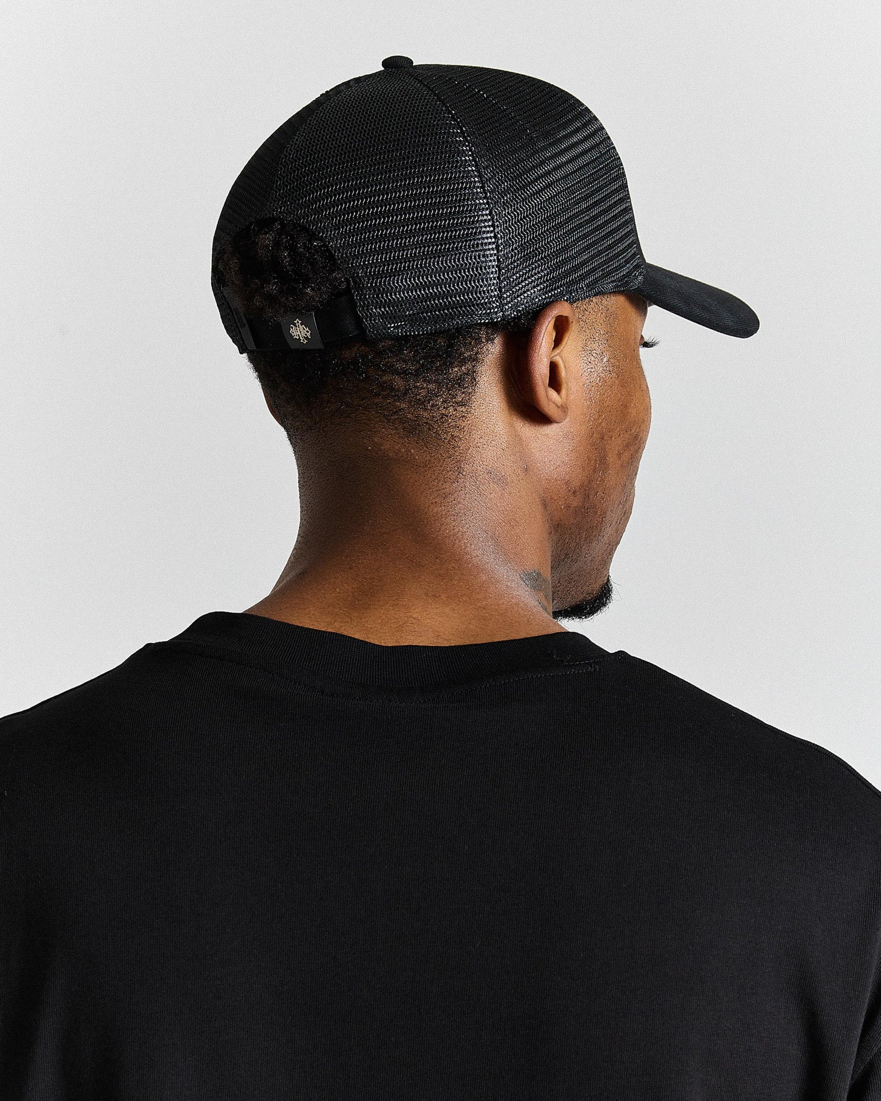 Person wearing a black trucker cap and black shirt on a light gray background