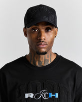 Man wearing a black cap and black shirt with visible branding on a gray background