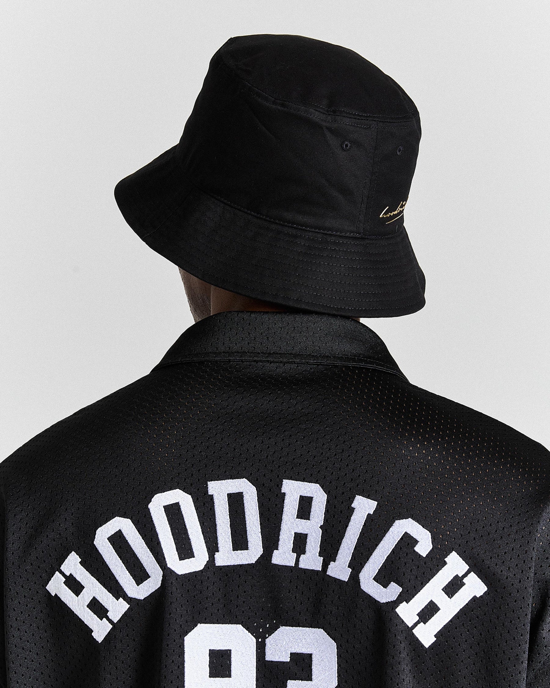 Person wearing a black bucket hat and black jacket with 'Hoodrich' text on a light gray background