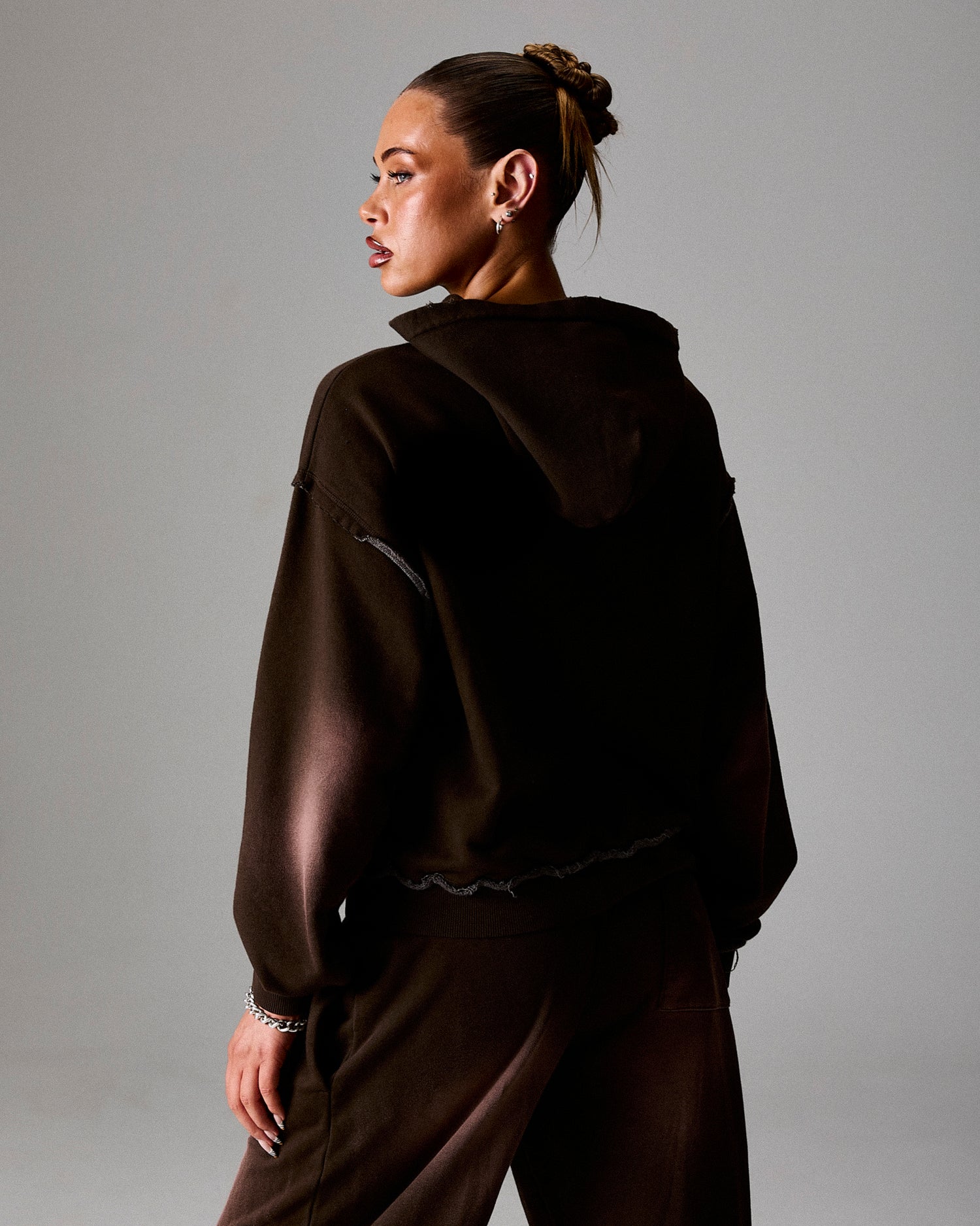 Person wearing a dark brown hoodie and pants against a gray background