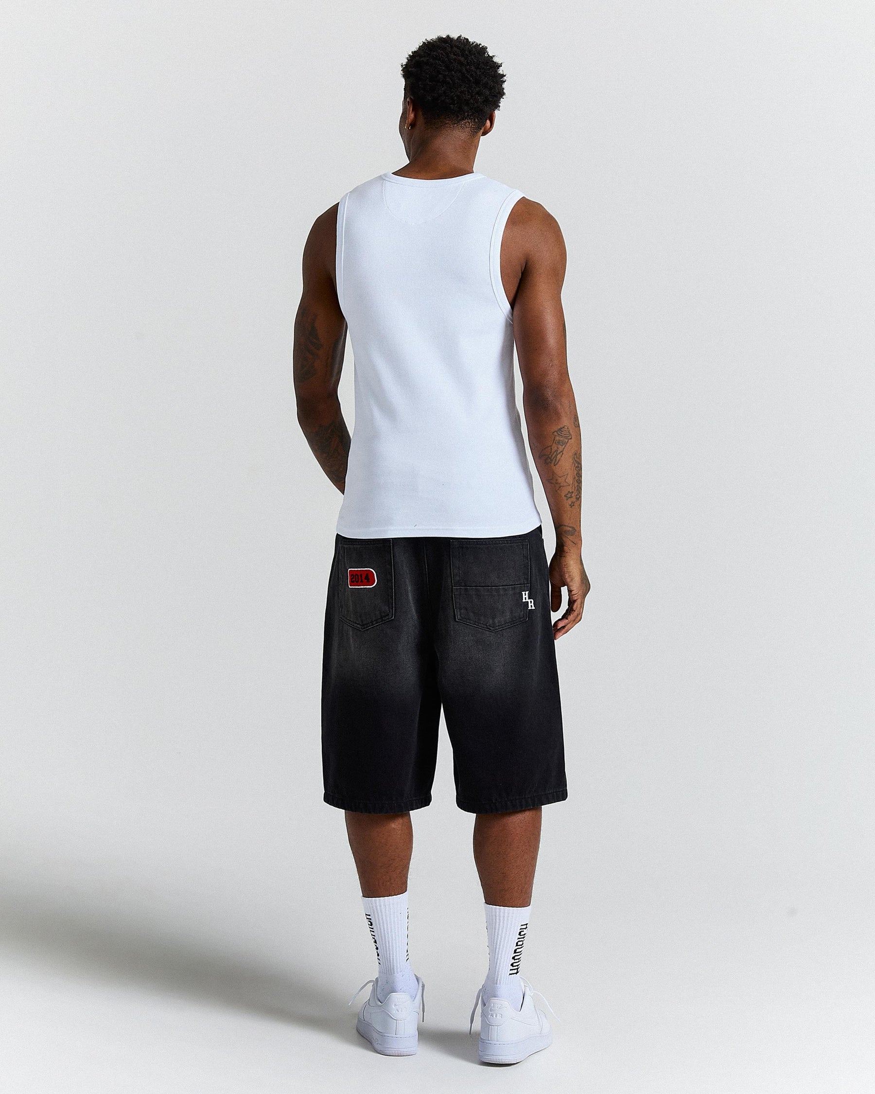 Person wearing a white tank top and black shorts on a light gray background