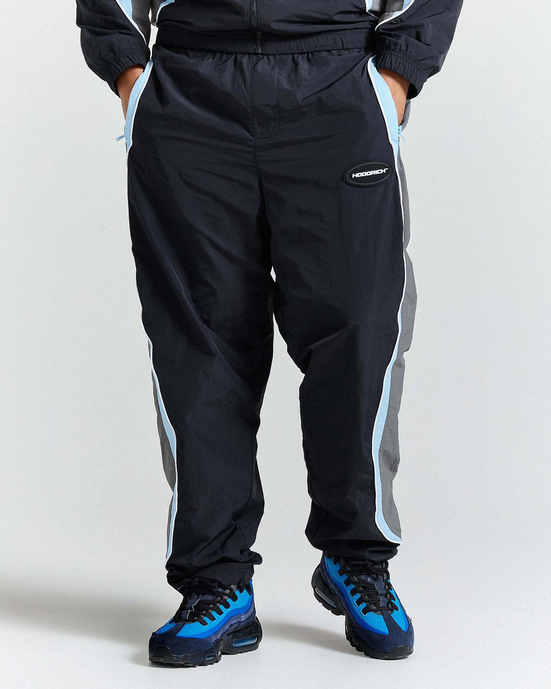 Person wearing black tracksuit with white and blue stripes on a plain background