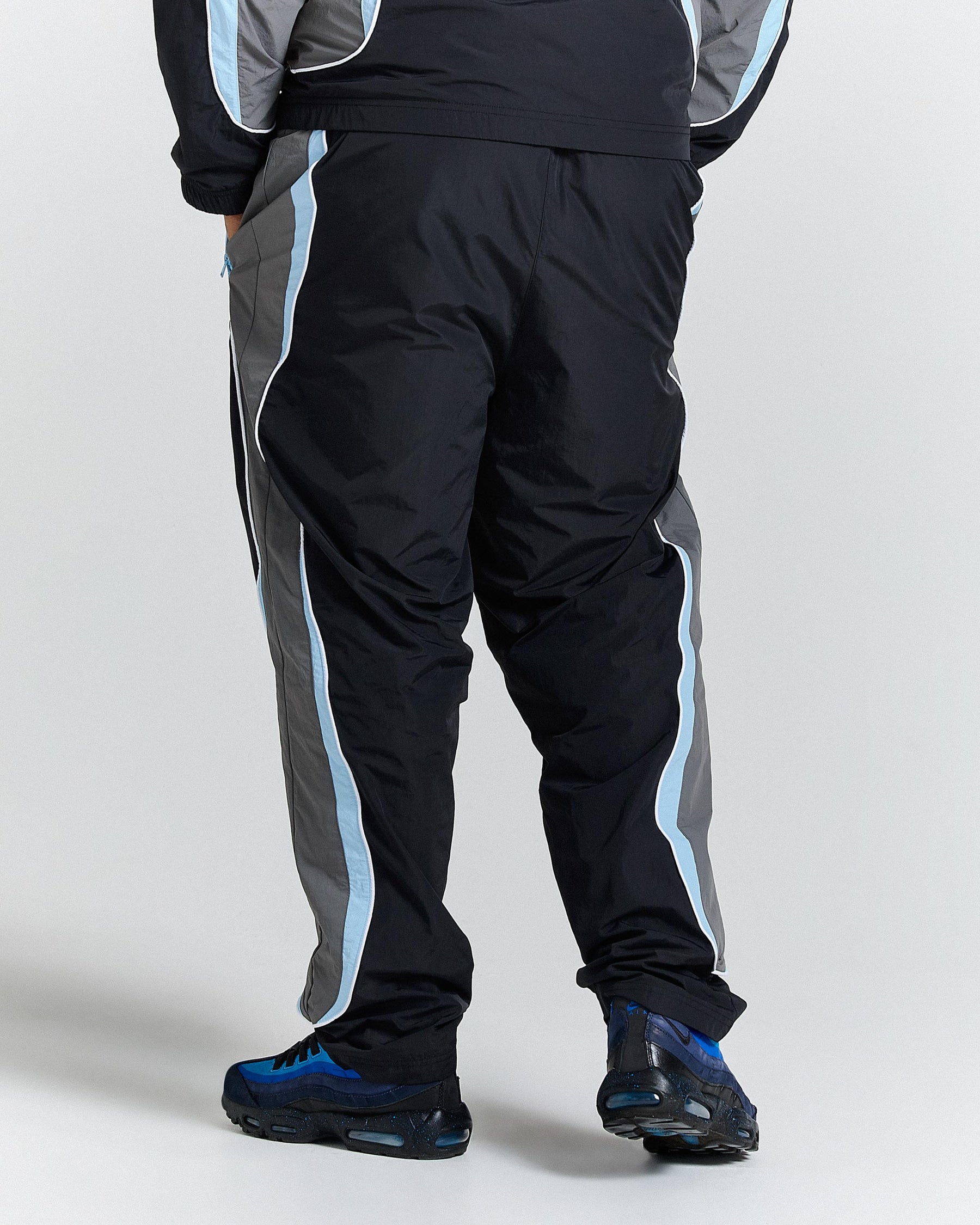 Person wearing black tracksuit with blue stripes on a white background