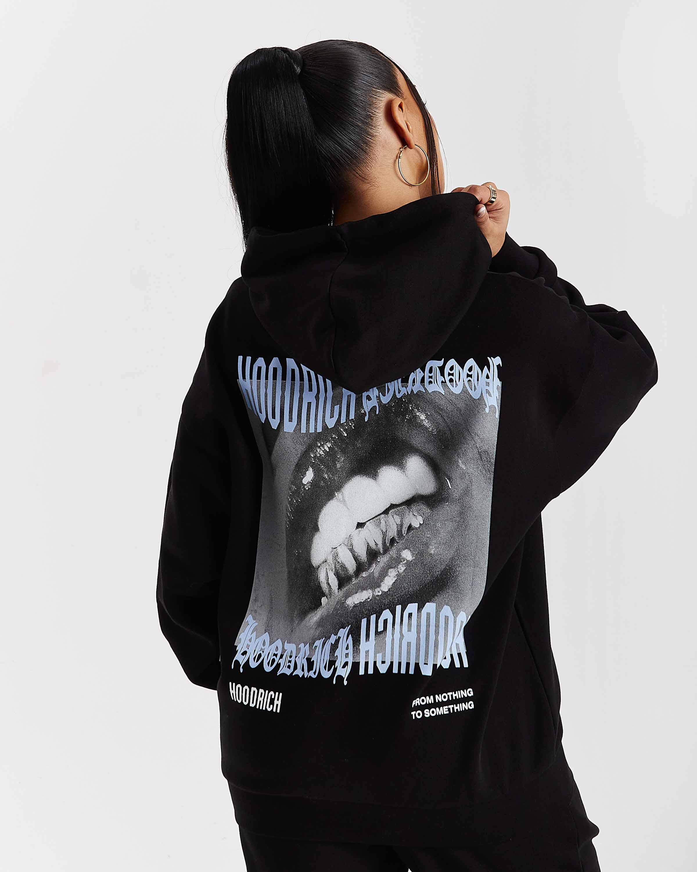 Person wearing a black hoodie with a graphic design on the back, standing against a plain background.