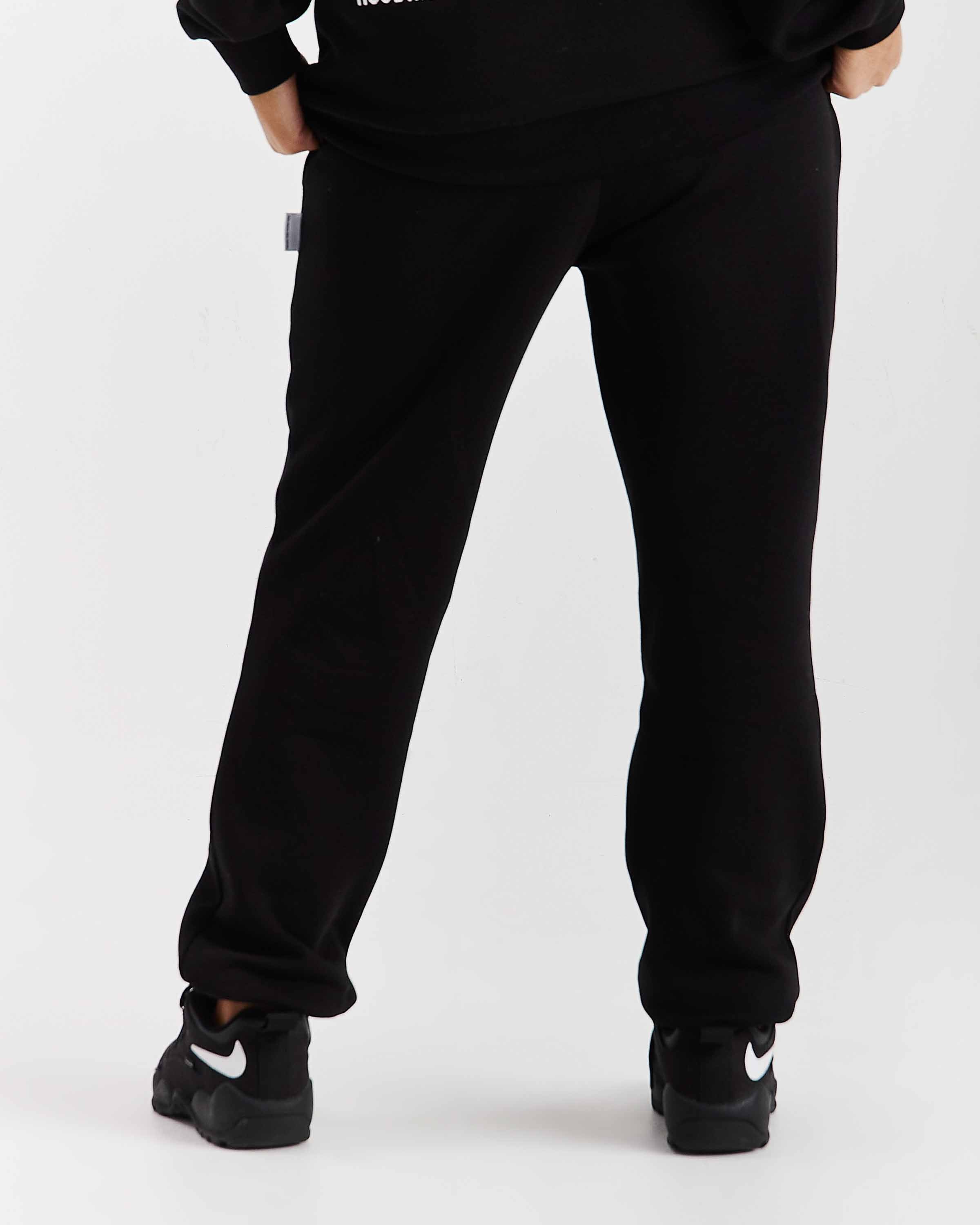 Person wearing black sweatpants and black Nike shoes on a white background