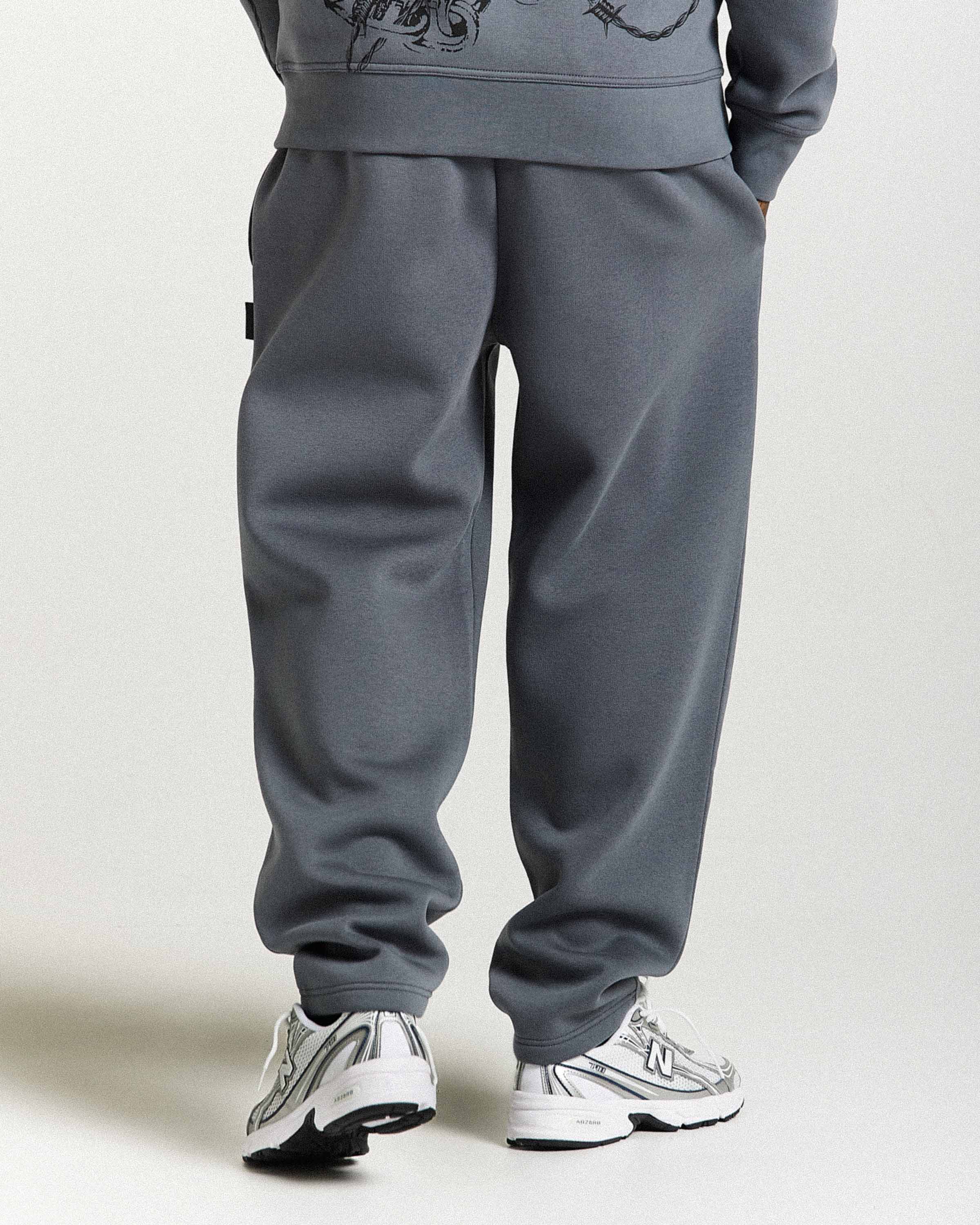 Person wearing gray sweatpants and sneakers on a plain background